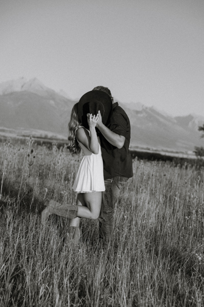 Rilee and Colby kissing playfully behind a cowboy hat during their Montana engagement session