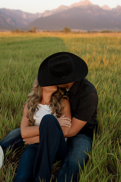 Rilee and Colby sitting in the grass, snuggled up and kissing during their Mission Valley engagement session