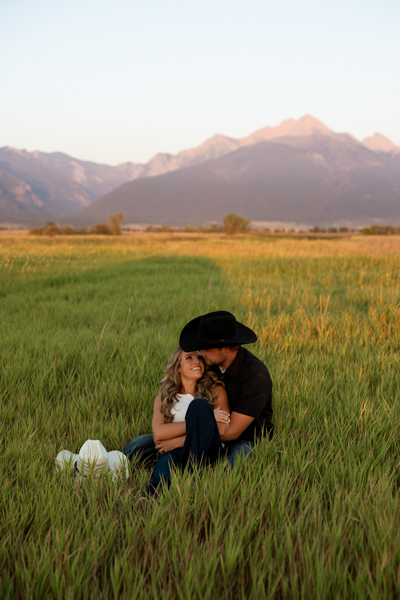 Rilee and Colby sitting close in the grass, smiling at each other during their Charlo Montana engagement session