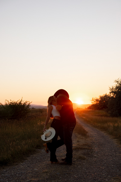 Rilee and Colby kissing during golden hour with Rilee’s foot kicked up and Mission Mountain views behind them