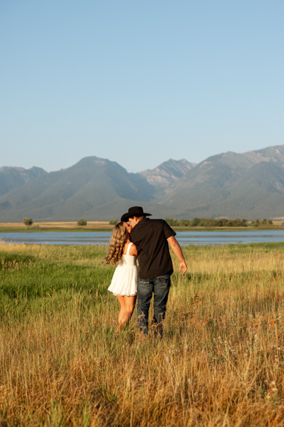 Rilee and Colby facing away from the camera sharing a kiss with Mission Mountain views in the background
