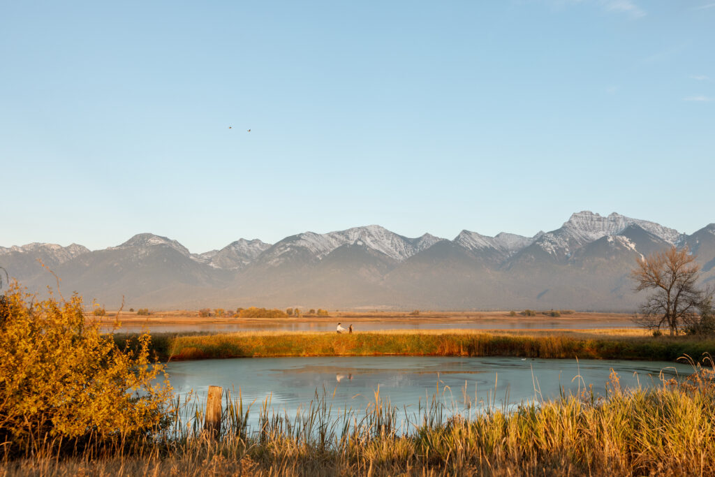 wide shot of couple on the other side of a pond with the mission mountains in the background