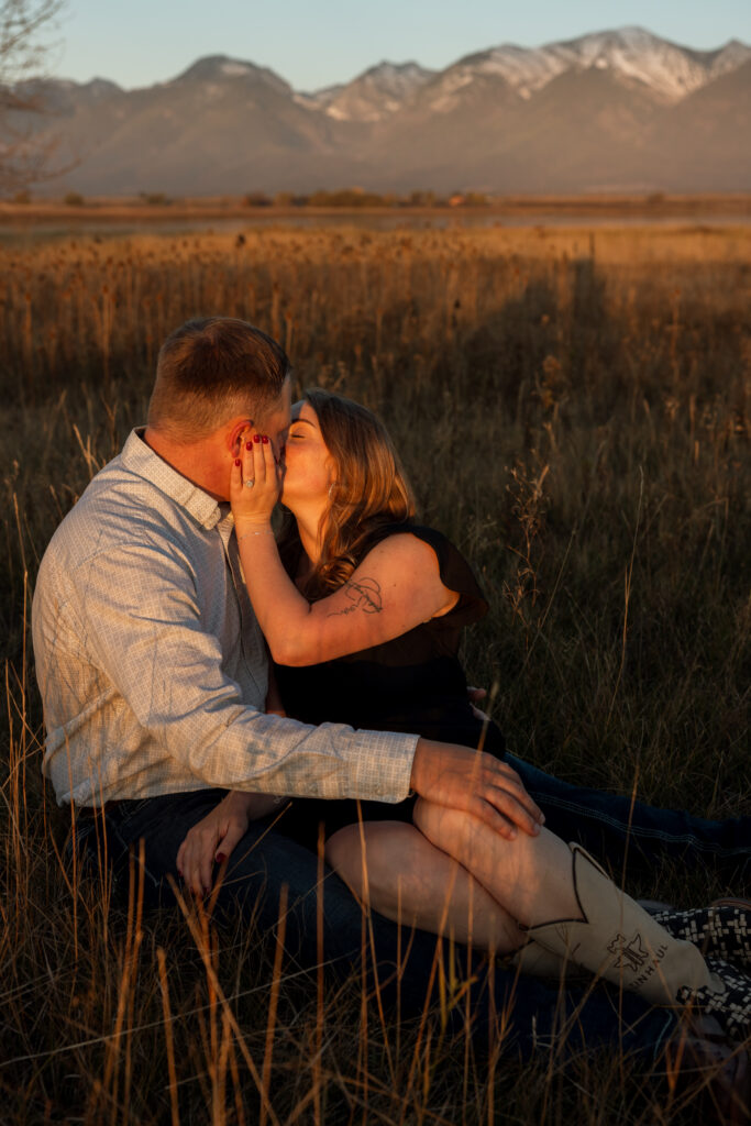 couple sitting on the ground kissing during a mission mountain engagement session
