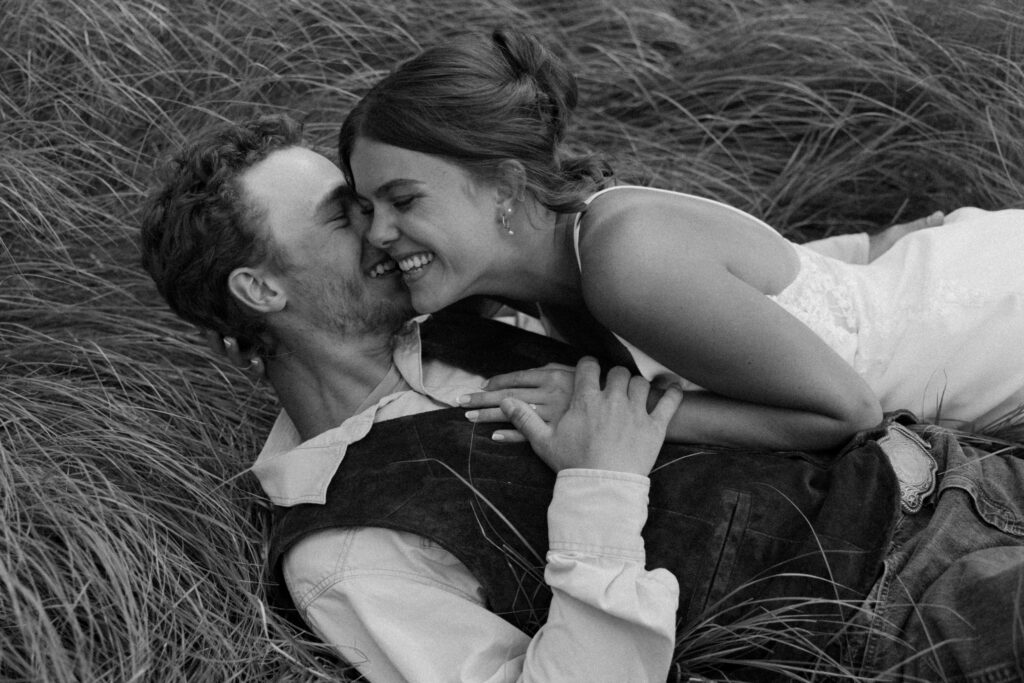 black and white photo of bride and groom laying in the grass laughing