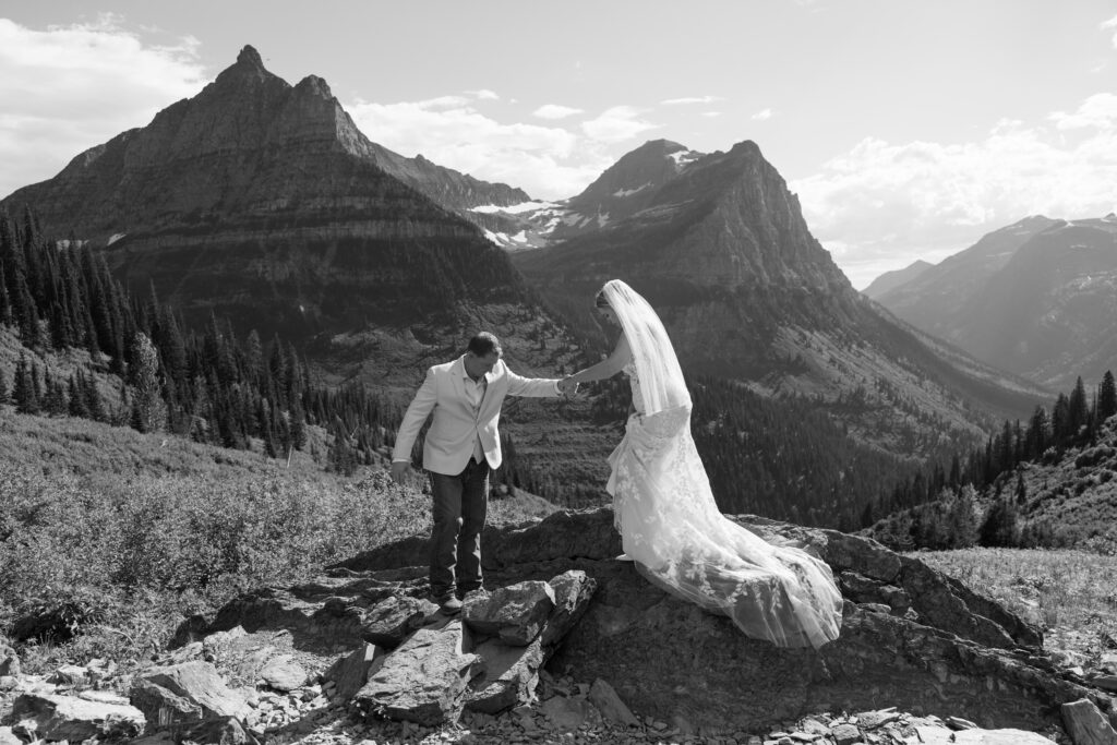 black and white photo of bride and groom climbing on the rock at big bend in glacier national park