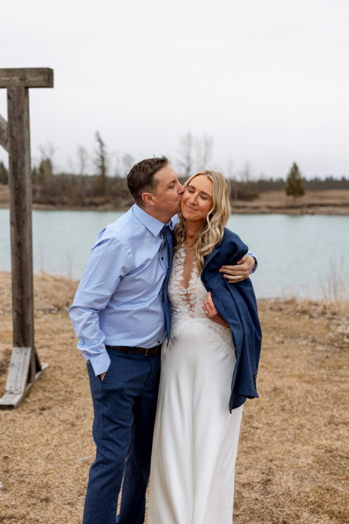 Groom wrapping tux jacket around bride while kissing her on the cheek at Diamond B Weddings — Kalispell Montana wedding photographer — Stacy Edwards Photography