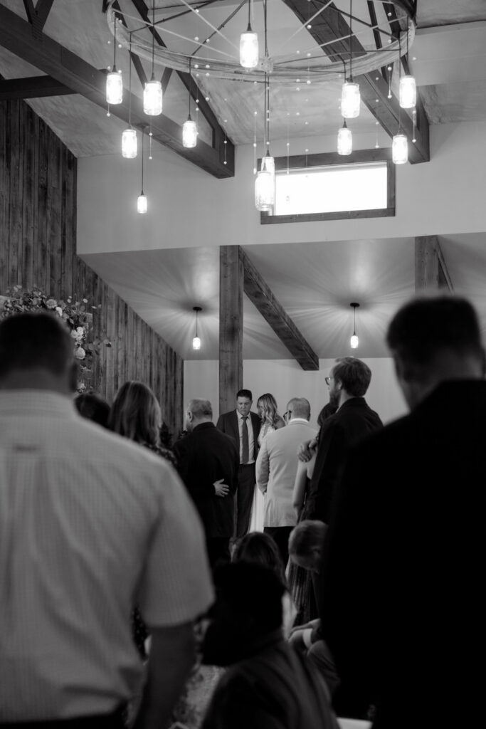 Bride and groom bowing in prayer while bride's father leads wedding prayer, shot through guests — Scott and Molly — Diamond B Weddings Kalispell Montana — Stacy Edwards Photography