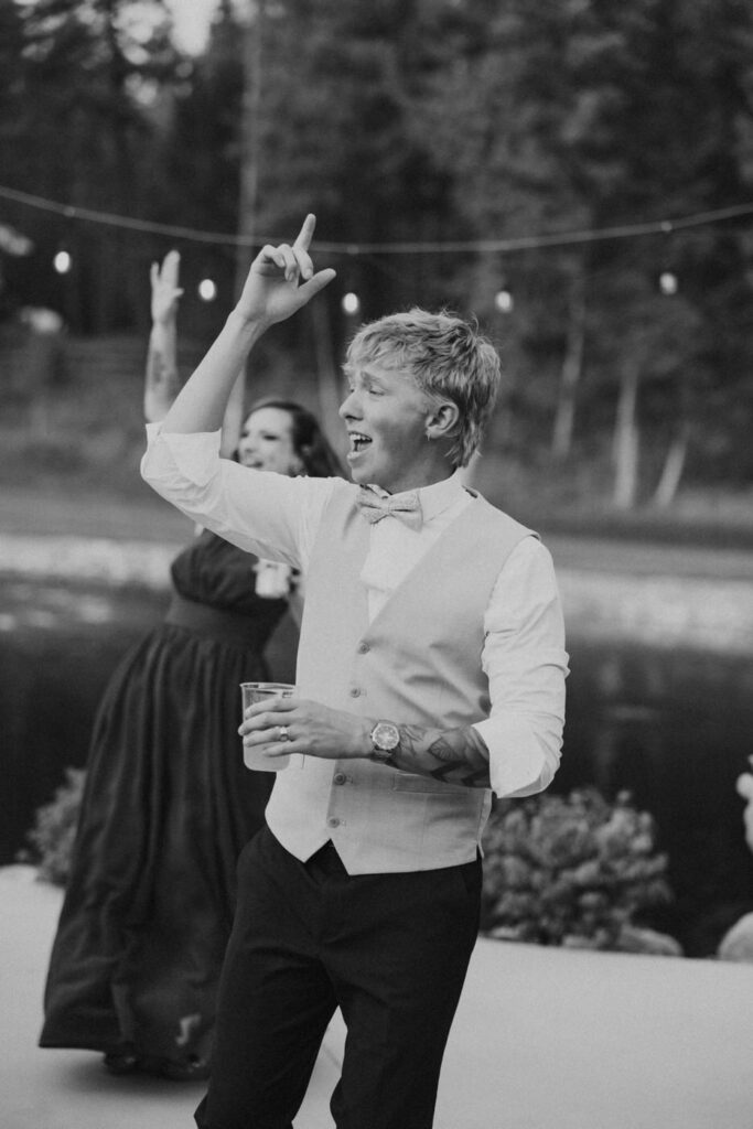 Black and white photo of groom dancing with hand pointed to the sky during Haymoon Resort wedding reception under string lights — Mikayla + Cayden — Haymoon Resort Wedding — Whitefish Montana — Stacy Edwards Photography