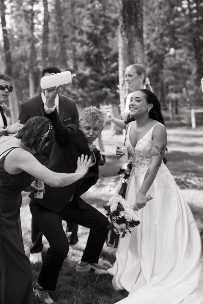 Black and white candid of wedding party celebrating and goofing around outside with the bride smiling and holding her bouquet — Mikayla + Cayden — Haymoon Resort Wedding — Whitefish Montana — Stacy Edwards Photography