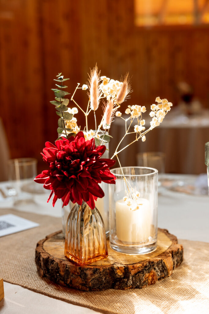 Close-up of rustic wedding centerpiece featuring a deep red dahlia, dried pampas grass, baby's breath, and eucalyptus on a wood slice with pillar candle — Mikayla + Cayden — Haymoon Resort Wedding — Whitefish Montana — Stacy Edwards Photography