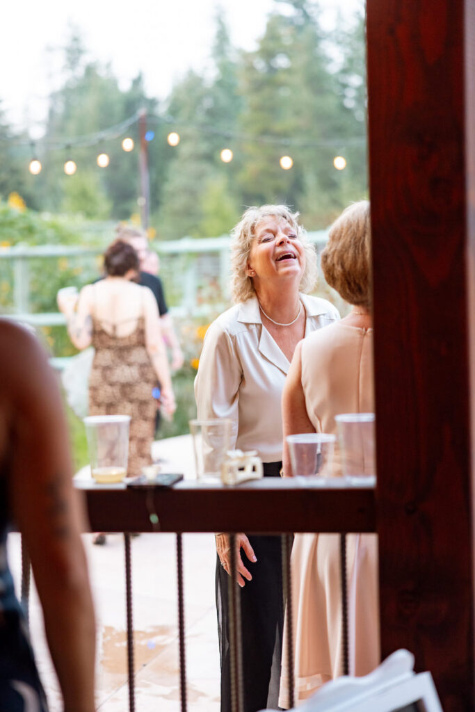 Wedding guest laughing with head thrown back during outdoor reception, string lights and pine trees in background — Mikayla + Cayden — Haymoon Resort Wedding — Whitefish Montana — Stacy Edwards Photography