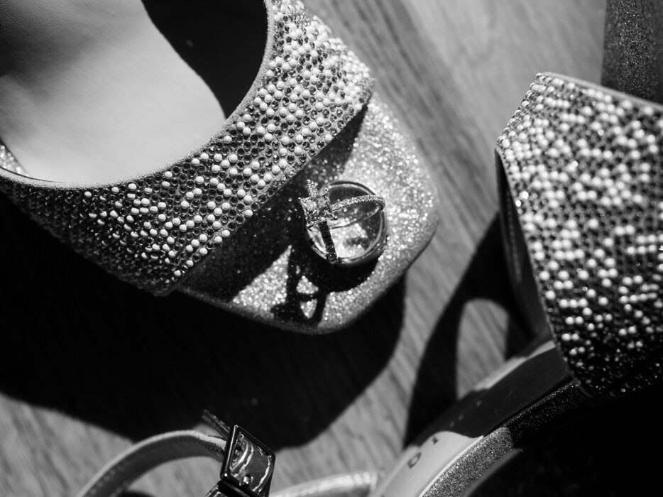 Black and white macro close-up of crystal-covered bridal heels with wedding ring resting against the buckle on a wood floor — Mikayla + Cayden — Haymoon Resort Wedding — Whitefish Montana — Stacy Edwards Photography