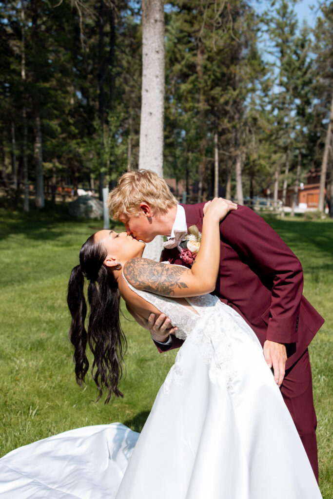 Groom dipping the bride for a kiss on the Haymoon Resort lawn, her dark hair cascading as Montana pine trees fill the background — Mikayla + Cayden — Haymoon Resort Wedding — Whitefish Montana — Stacy Edwards Photography