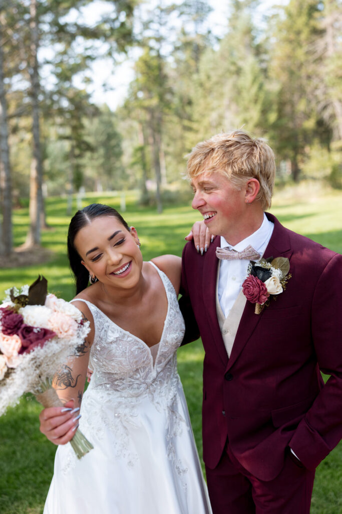 Bride and groom laughing together during portraits on the Haymoon Resort lawn, she leaning against his shoulder with bouquet in hand — Mikayla + Cayden — Haymoon Resort Wedding — Whitefish Montana — Stacy Edwards Photography