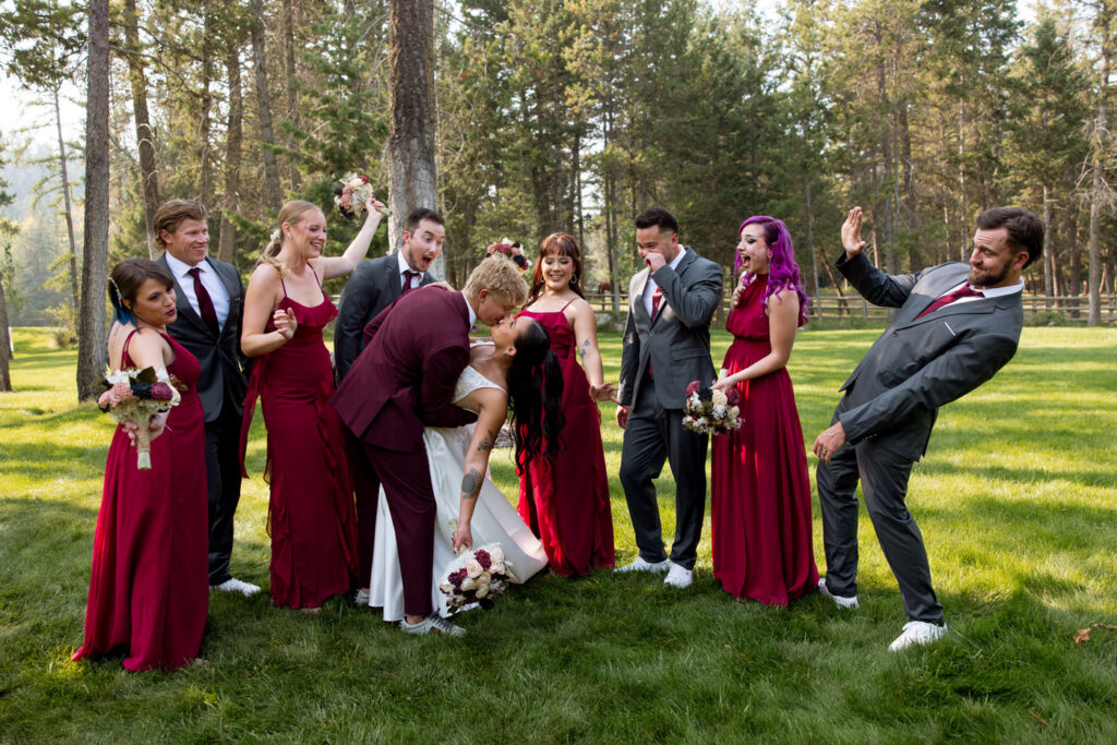 Full wedding party photo with groom dipping bride for a kiss surrounded by cheering bridesmaids and groomsmen on the Haymoon Resort lawn — Mikayla + Cayden — Haymoon Resort Wedding — Whitefish Montana — Stacy Edwards Photography