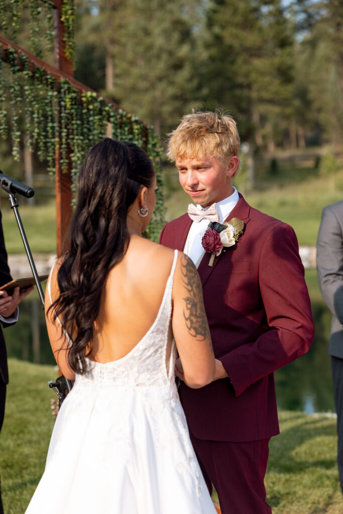 Groom looking emotionally at his bride during vow exchange at the Haymoon Resort ceremony, the pond and pine trees visible behind him — Mikayla + Cayden — Haymoon Resort Wedding — Whitefish Montana — Stacy Edwards Photography