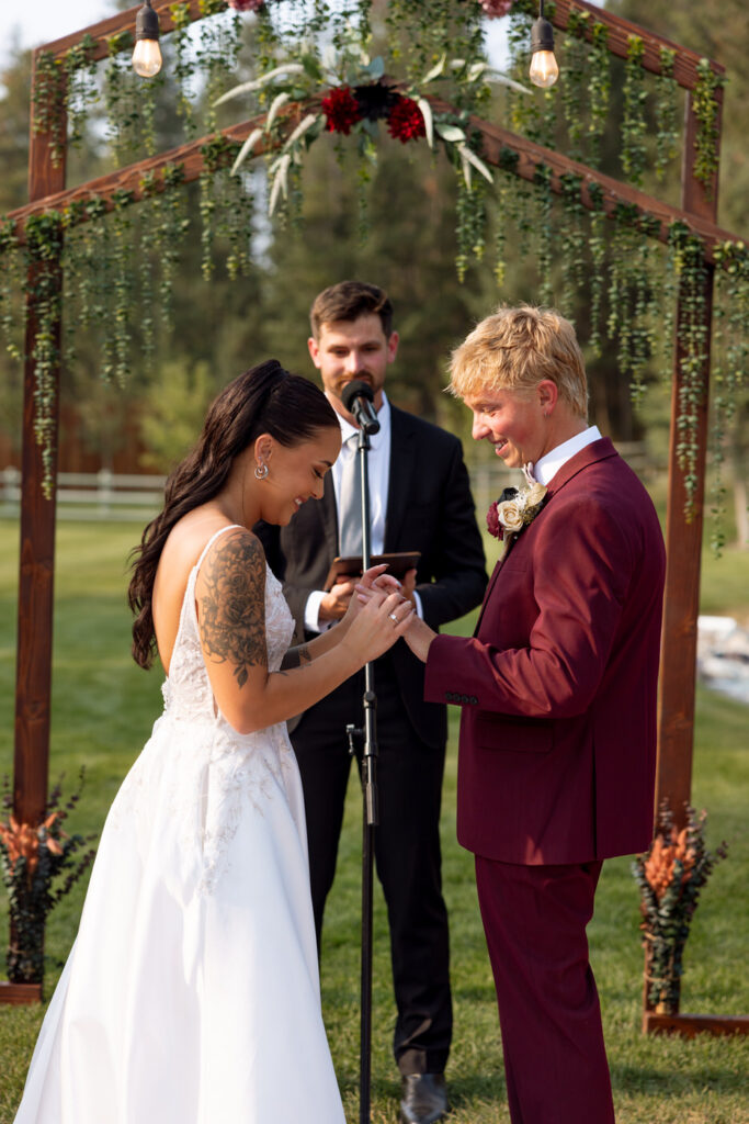 Bride sliding the wedding ring onto the groom's finger during the ring exchange at the Haymoon Resort outdoor ceremony, both looking down and smiling — Mikayla + Cayden — Haymoon Resort Wedding — Whitefish Montana — Stacy Edwards Photography