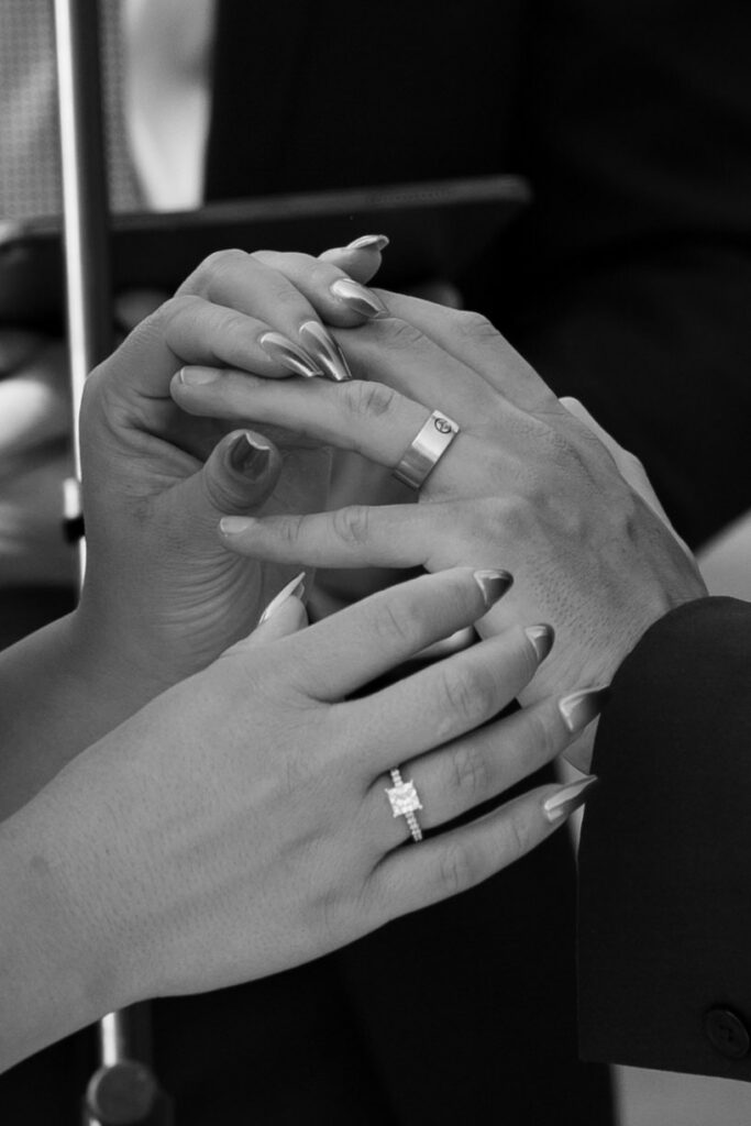 Black and white close-up of bride and groom's hands intertwined after the ring exchange, her princess-cut engagement ring and his wedding band visible — Mikayla + Cayden — Haymoon Resort Wedding — Whitefish Montana — Stacy Edwards Photography