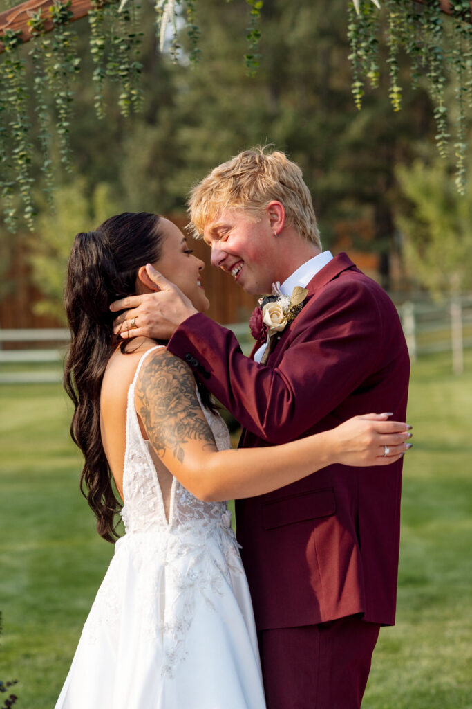 Groom cradling bride's face as they lean in nose to nose after the ceremony beneath the Haymoon Resort greenery arch, both laughing with eyes nearly closed — Mikayla + Cayden — Haymoon Resort Wedding — Whitefish Montana — Stacy Edwards Photography