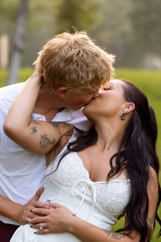 Close portrait of bride and groom kissing during sunset reception portraits on the Haymoon Resort lawn, her floral arm tattoo and his sleeve tattoo both visible — Mikayla + Cayden — Haymoon Resort Wedding — Whitefish Montana — Stacy Edwards Photography