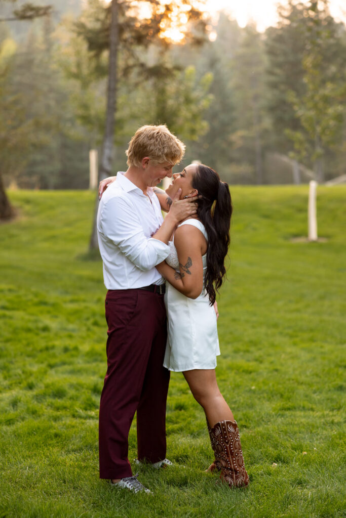 Bride and groom nearly touching foreheads in a tender moment on the green Montana lawn at golden hour, she in white reception mini dress and cowboy boots — Mikayla + Cayden — Haymoon Resort Wedding — Whitefish Montana — Stacy Edwards Photography