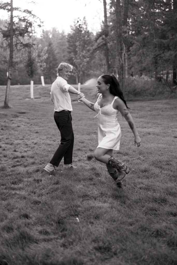 Black and white photo of bride and groom dancing and spinning together on the Haymoon Resort lawn at dusk, she in her white mini dress and western boots — Mikayla + Cayden — Haymoon Resort Wedding — Whitefish Montana — Stacy Edwards Photography