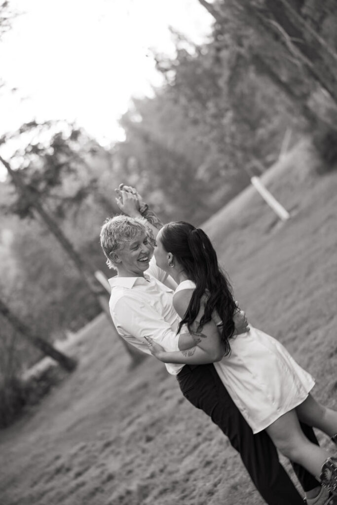 Black and white photo of groom spinning bride in a joyful dance on the Montana lawn at Haymoon Resort, both laughing as she lifts off the ground — Mikayla + Cayden — Haymoon Resort Wedding — Whitefish Montana — Stacy Edwards Photography