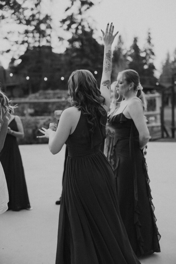 Black and white reception dance floor photo of bridesmaids in long black dresses, one with arm raised and tattoos visible — Mikayla + Cayden — Haymoon Resort Wedding — Whitefish Montana — Stacy Edwards Photography