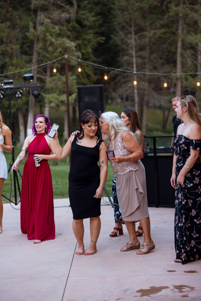 Candid of guests dancing on the Haymoon Resort outdoor dance floor at dusk, an older woman giving a kiss on the cheek to a guest in a black dress near the DJ — Mikayla + Cayden — Haymoon Resort Wedding — Whitefish Montana — Stacy Edwards Photography