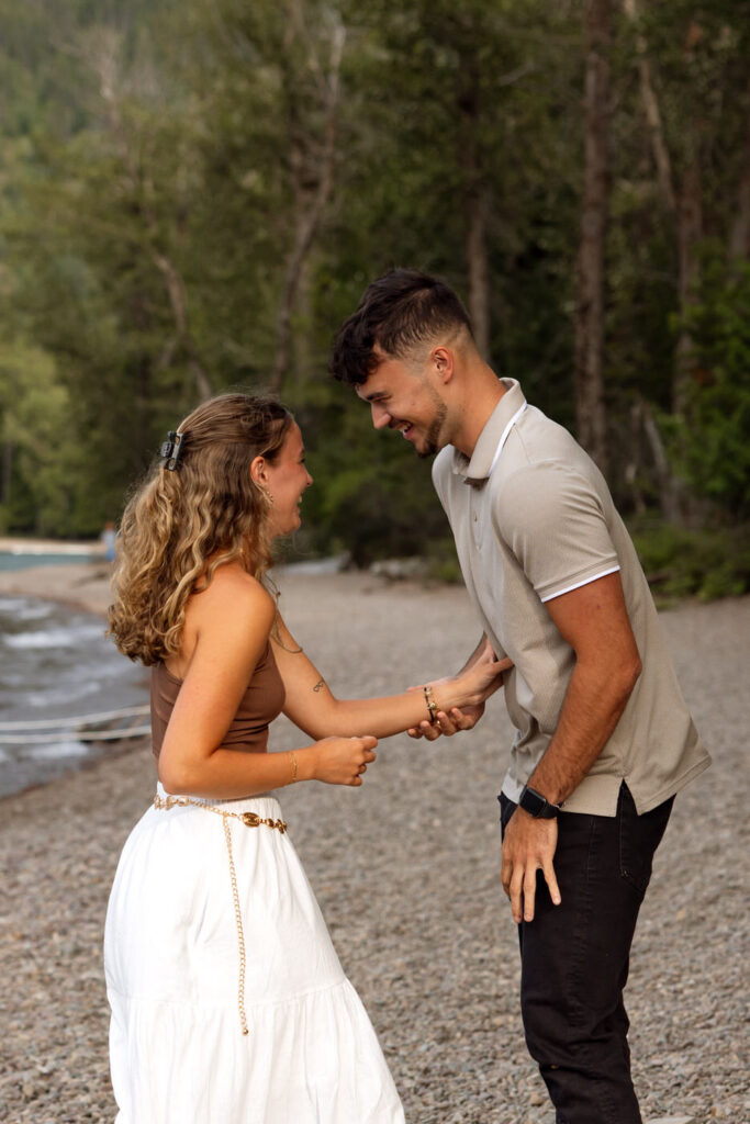 Close-up of engaged couple smiling and laughing face to face on the pebbled beach at Lake McDonald — Ryan + Liz — Surprise Proposal — Glacier National Park — Stacy Edwards Photography
