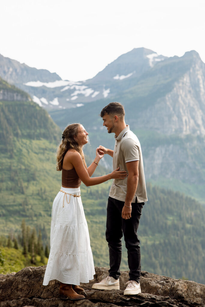 Newly engaged couple laughing together on a rocky overlook at Big Bend, Going to the Sun Road, Glacier National Park — Ryan + Liz — Surprise Proposal — Glacier National Park — Stacy Edwards Photography