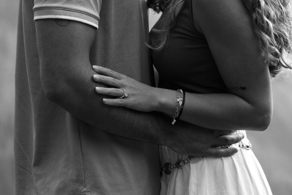 Black and white close-up of newly engaged woman's hand showing engagement ring while embracing her partner — Ryan + Liz — Surprise Proposal — Glacier National Park — Stacy Edwards Photography