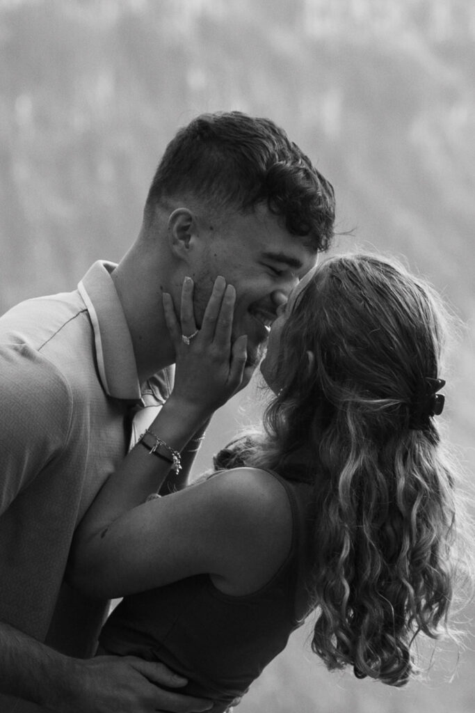 Black and white close-up of newly engaged couple sharing a tender almost-kiss, engagement ring visible on her hand, Glacier National Park — Ryan + Liz — Surprise Proposal — Glacier National Park — Stacy Edwards Photography