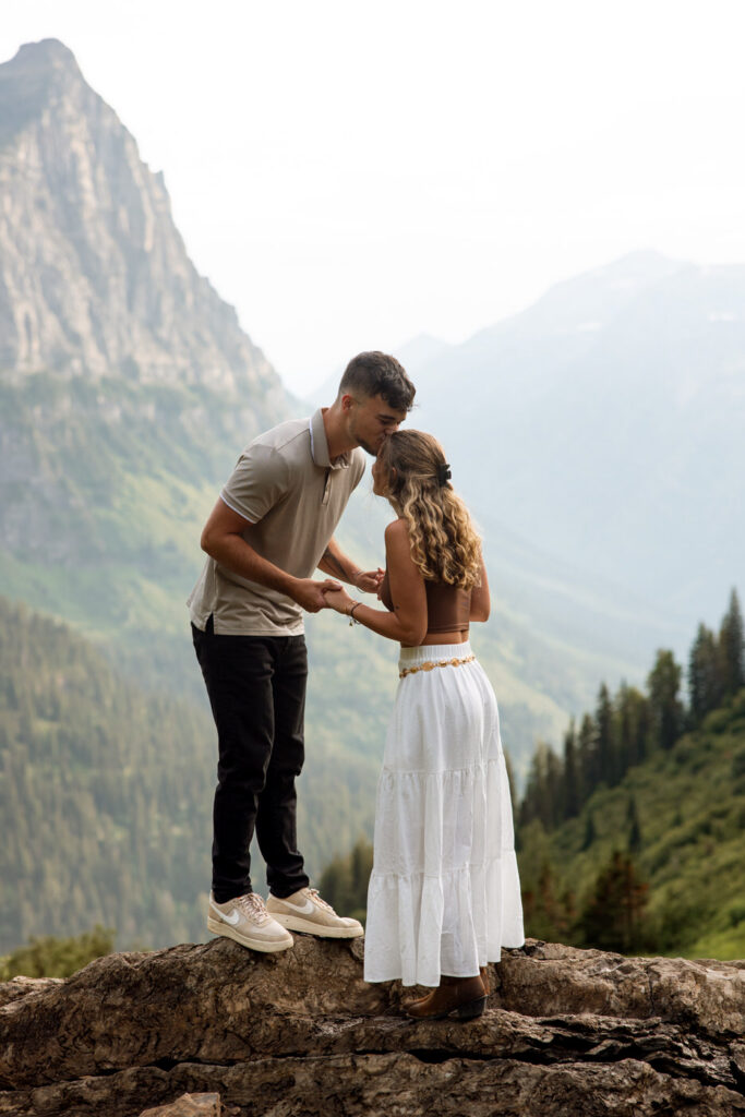 Man kissing woman's forehead while admiring her engagement ring on a rocky overlook along Going to the Sun Road, Glacier National Park — Ryan + Liz — Surprise Proposal — Glacier National Park — Stacy Edwards Photography