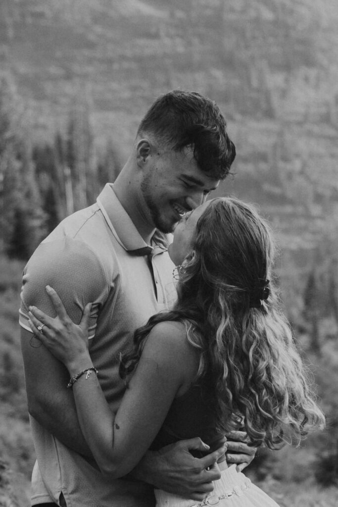 Black and white close-up of engaged couple nearly kissing, engagement ring visible, Glacier National Park mountain backdrop — Ryan + Liz — Surprise Proposal — Glacier National Park — Stacy Edwards Photography