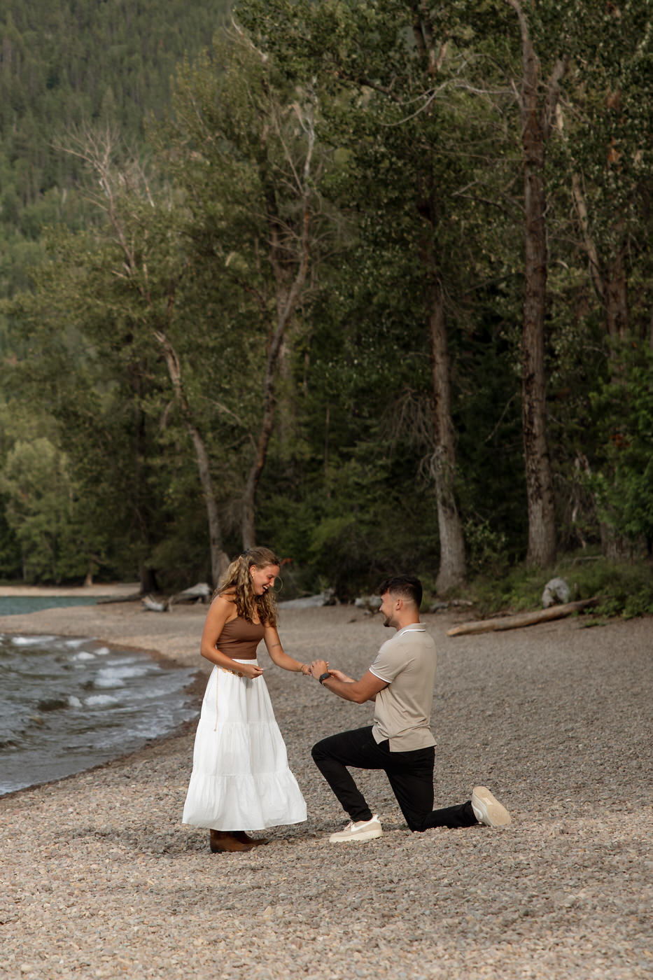 Man on one knee proposing to woman on the pebbled beach at Apgar Village, Lake McDonald — Ryan + Liz — Surprise Proposal — Glacier National Park — Stacy Edwards Photography