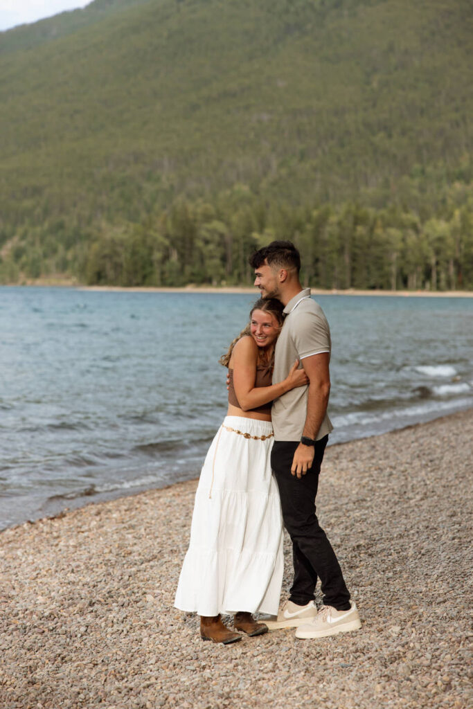 Engaged couple embracing on the rocky shoreline of Lake McDonald, Glacier National Park — Ryan + Liz — Surprise Proposal — Glacier National Park — Stacy Edwards Photography