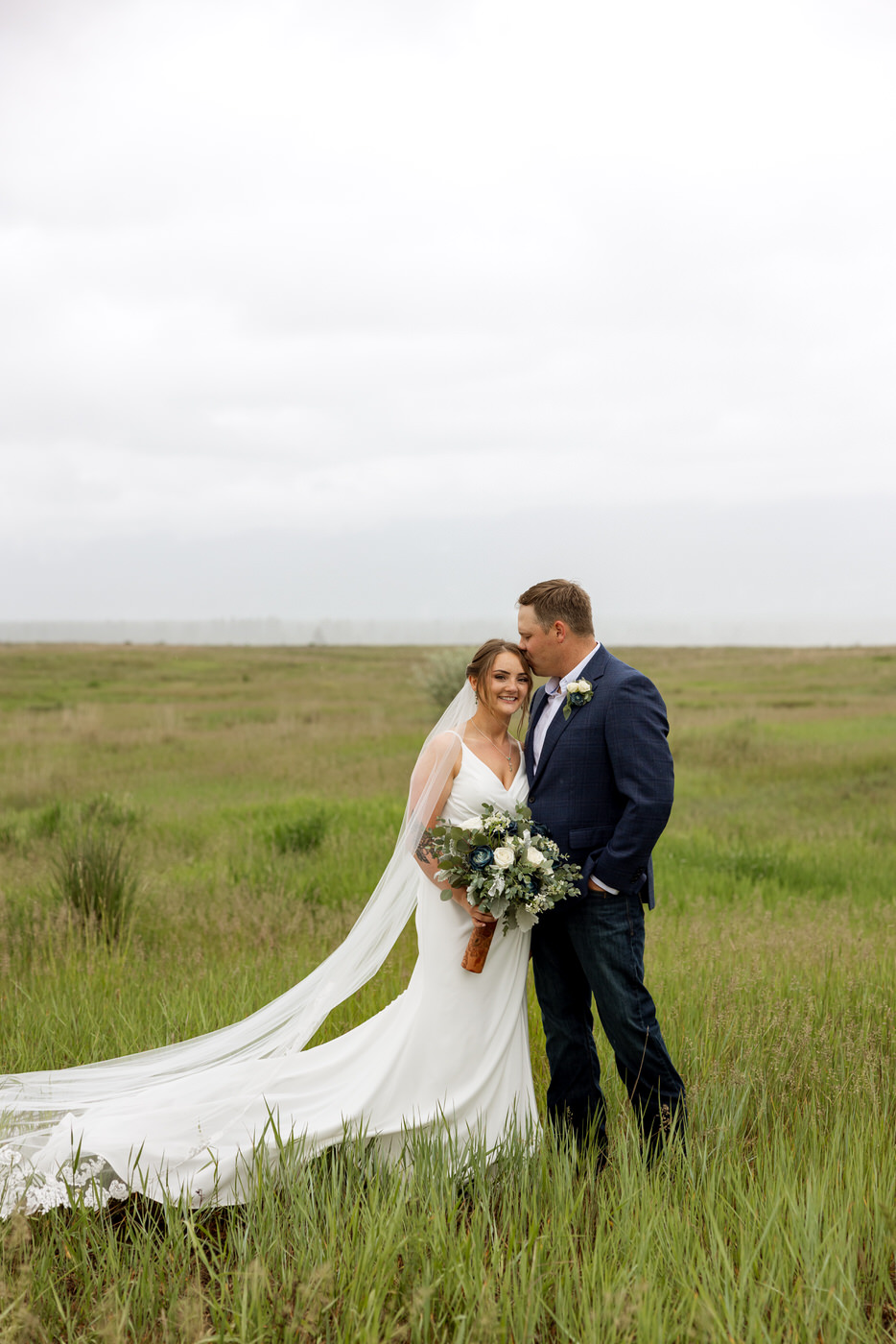 Bride smiling at the camera while groom kisses her on the side of the head — Aislynn + Kyle — Mission Valley Wedding — Charlo Montana — Stacy Edwards Photography