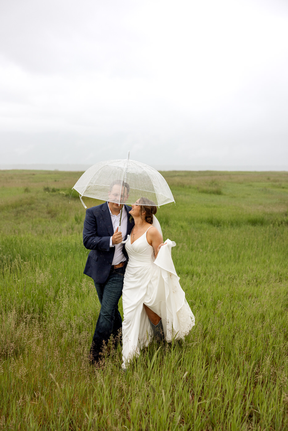 Bride and groom walking and giggling, snuggled in close under an umbrella — Aislynn + Kyle — Mission Valley Wedding — Charlo Montana — Stacy Edwards Photography