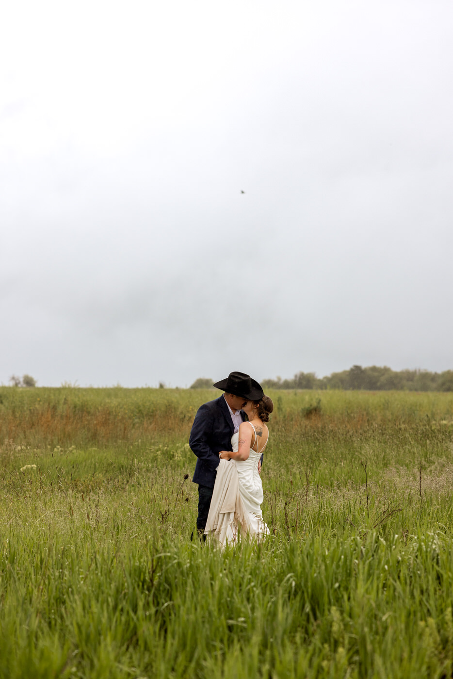 Wide shot of bride and groom kissing in a grassy field — Aislynn + Kyle — Mission Valley Wedding — Charlo Montana — Stacy Edwards Photography