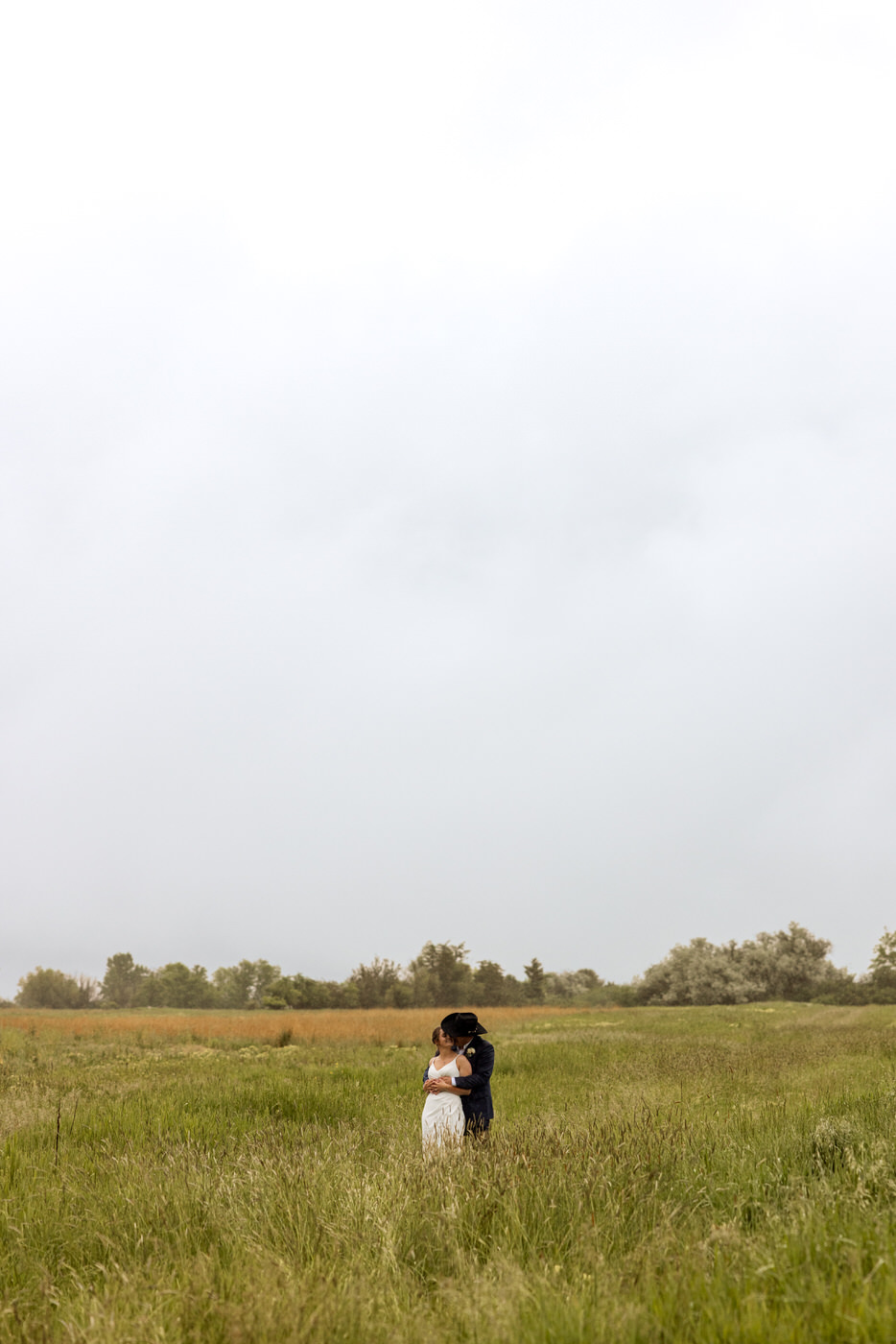Really wide shot of bride and groom in an embrace in a grassy field — Aislynn + Kyle — Mission Valley Wedding — Charlo Montana — Stacy Edwards Photography