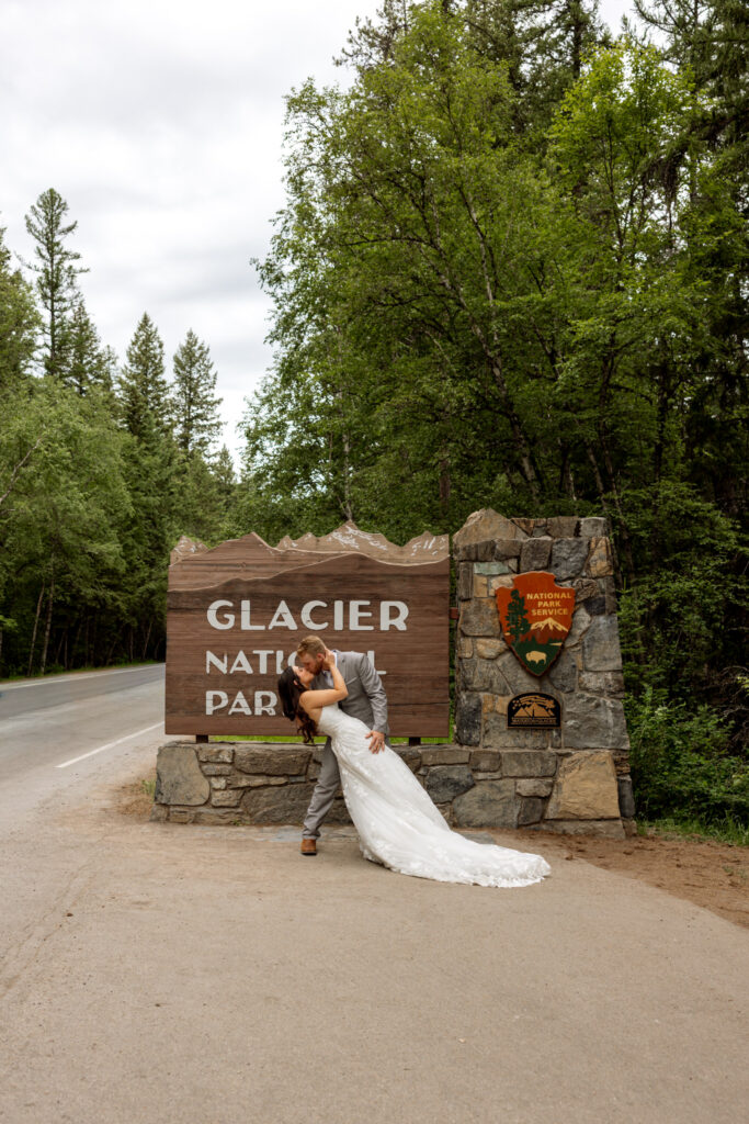 Groom dipping bride in front of the Glacier National Park entrance sign — Glacier National Park wedding photographer Stacy Edwards Photography
