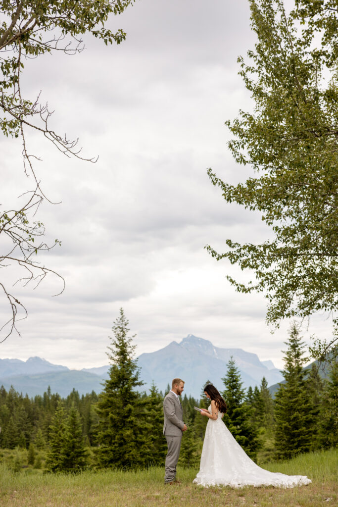 Bride reading private vows to groom in an open meadow with Glacier National Park mountains in the background — Glacier National Park elopement photographer Stacy Edwards Photography