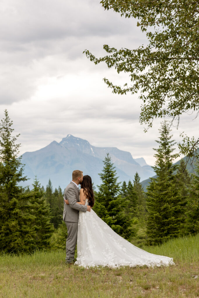 Bride and groom embracing back to camera in a meadow with mountain peak behind them — Belton Stage Park Glacier National Park elopement — Stacy Edwards Photography