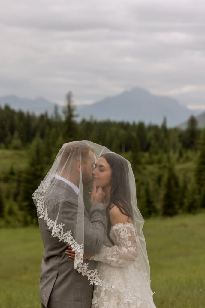 Bride and groom nose to nose under lace veil in a rainy meadow near Glacier National Park — Glacier National Park elopement photographer Stacy Edwards Photography