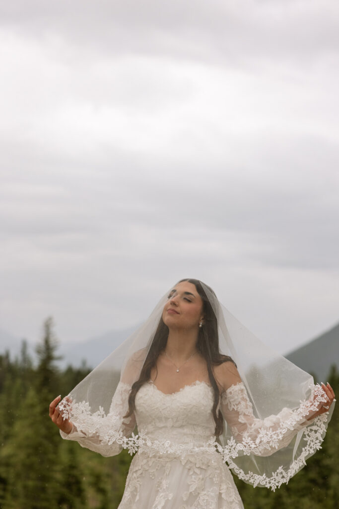 Bride holding lace veil wide open looking up at the sky in a mountain meadow — Glacier National Park elopement — Stacy Edwards Photography