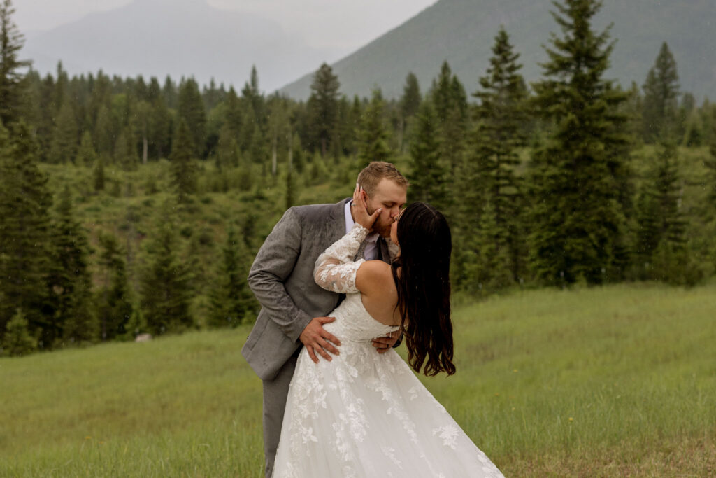Groom dipping bride for a kiss in a rainy green meadow near Glacier National Park — Belton Stage Park elopement — Stacy Edwards Photography