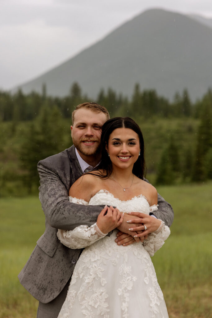 Bride and groom smiling at camera in a rainy mountain meadow near West Glacier Montana — Glacier National Park elopement photographer Stacy Edwards Photography