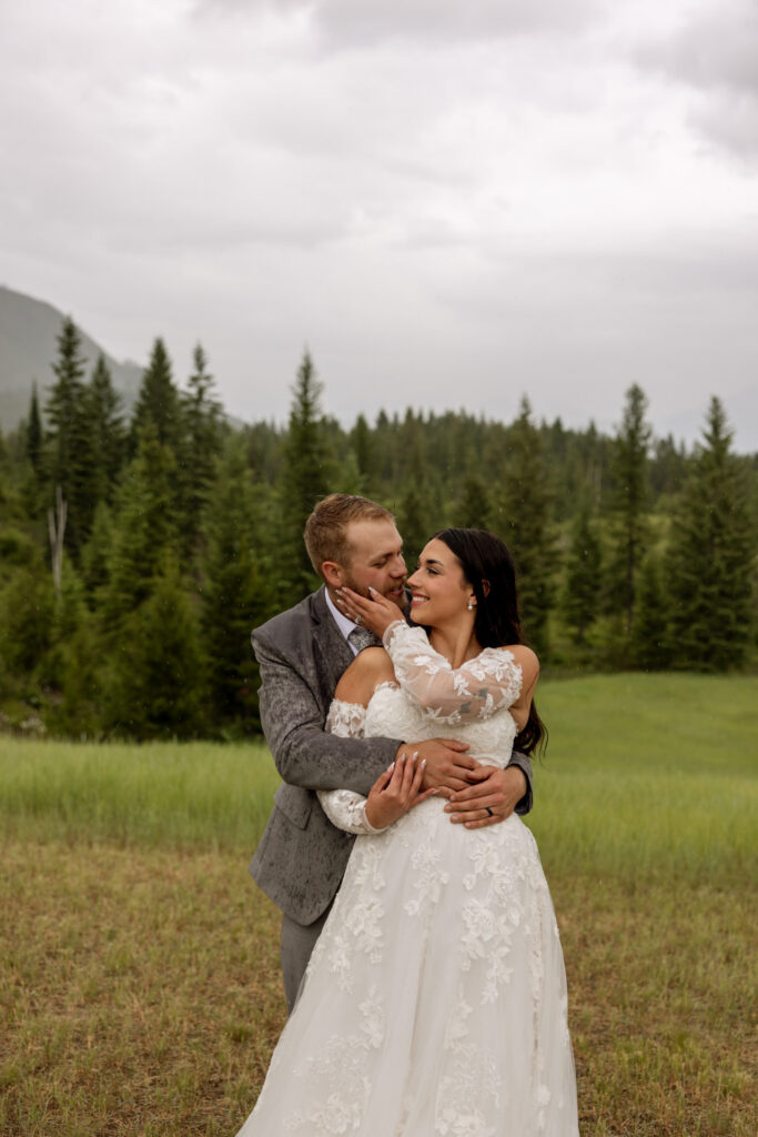 Groom nuzzling bride from behind while she smiles in a pine tree meadow near West Glacier — Glacier National Park elopement photographer Stacy Edwards Photography