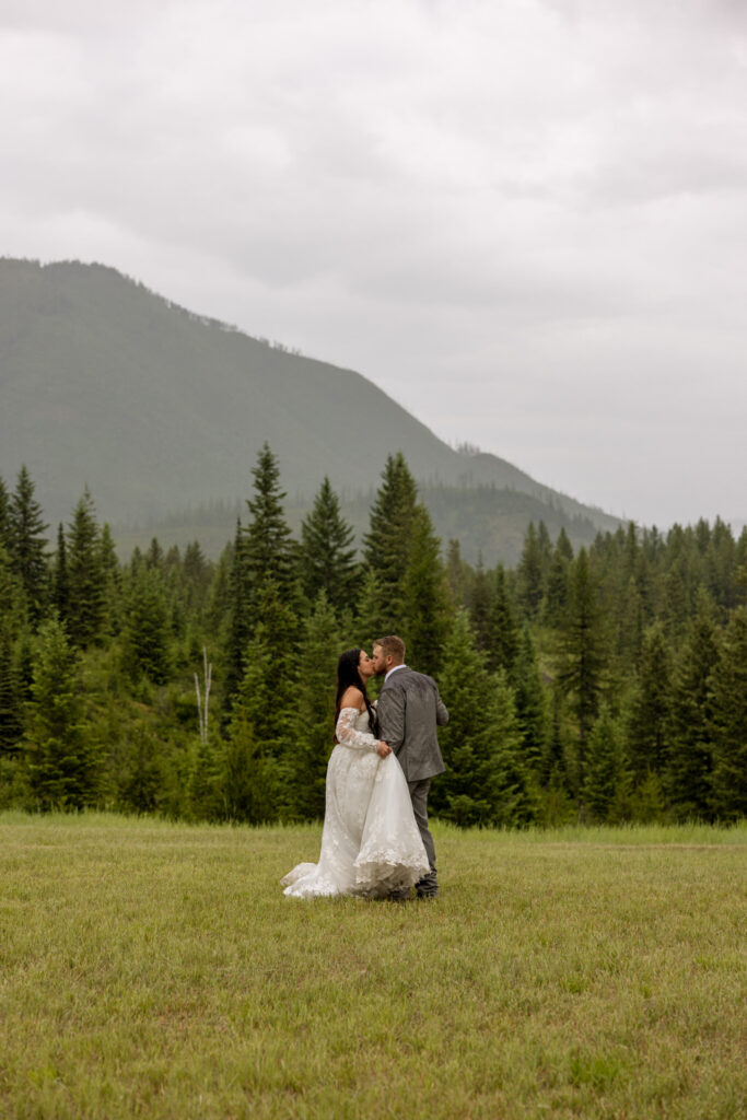 Bride and groom kissing in a wide open mountain meadow at Belton Stage Park near West Glacier Montana — Glacier National Park elopement — Stacy Edwards Photography